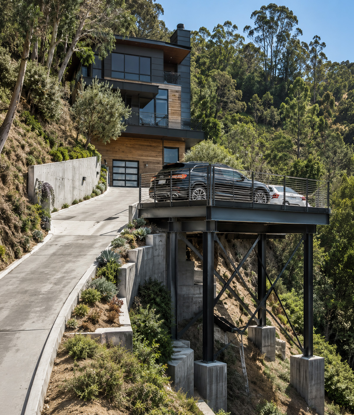 Modern hillside home with an elevated parking deck connected to a sloped driveway, supported by steel columns, cross-bracing, and concrete footings for a structurally engineered parking solution.