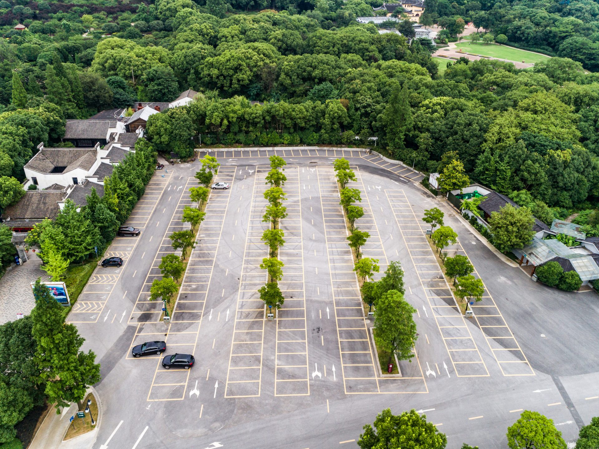 Elevated residential parking deck under construction on a steep hillside lot, with exposed steel beams, concrete footings, structural bracing, workers, materials, and a driveway ramp connection.
